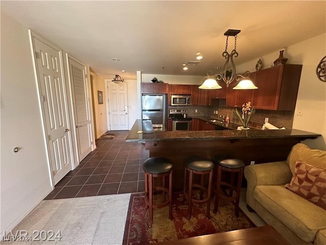 kitchen with kitchen peninsula, tasteful backsplash, stainless steel appliances, dark tile patterned floors, and pendant lighting