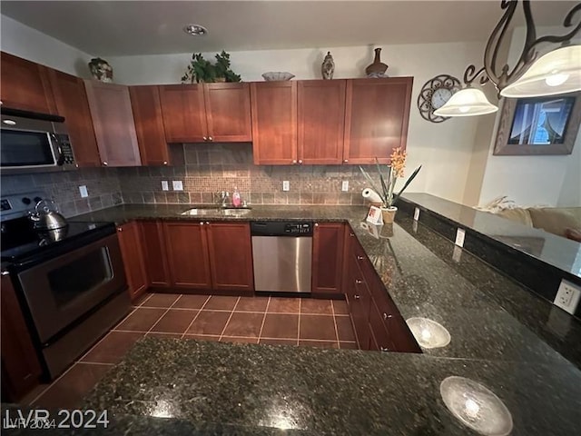 kitchen with sink, hanging light fixtures, dark stone countertops, appliances with stainless steel finishes, and tasteful backsplash