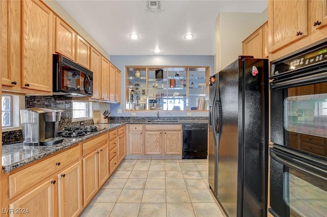 kitchen featuring light tile patterned floors, dark stone countertops, a healthy amount of sunlight, and black appliances