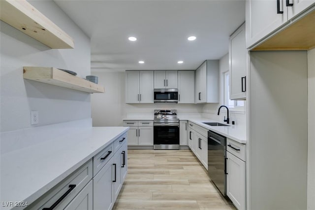 kitchen with appliances with stainless steel finishes, light hardwood / wood-style flooring, white cabinetry, and sink