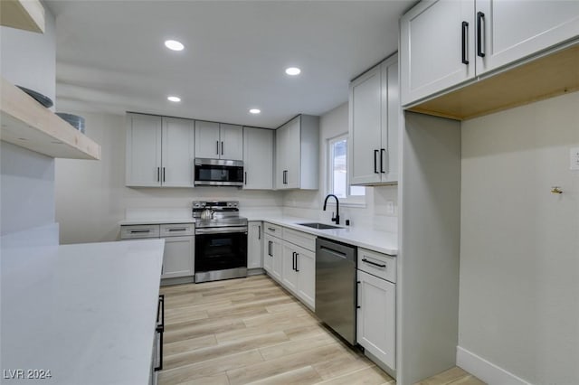 kitchen with sink, white cabinets, light hardwood / wood-style flooring, and appliances with stainless steel finishes