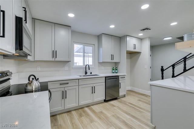 kitchen featuring light stone countertops, light wood-type flooring, stainless steel appliances, and sink