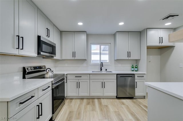 kitchen featuring white cabinets, light wood-type flooring, stainless steel appliances, and sink