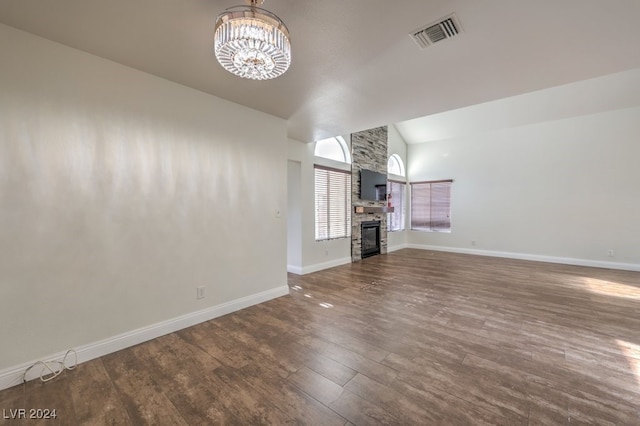 unfurnished living room with a stone fireplace, dark hardwood / wood-style flooring, a chandelier, and vaulted ceiling