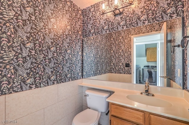 bathroom featuring vanity, separate washer and dryer, toilet, and tile walls