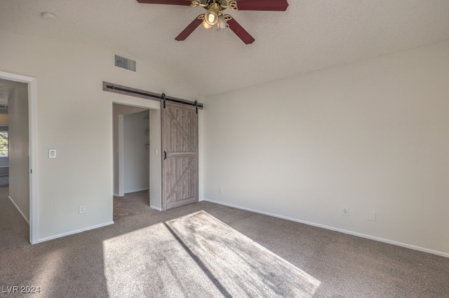 unfurnished bedroom featuring ceiling fan, a spacious closet, a barn door, vaulted ceiling, and carpet