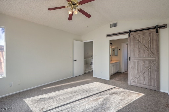 unfurnished bedroom featuring ensuite bath, a textured ceiling, light colored carpet, ceiling fan, and a barn door