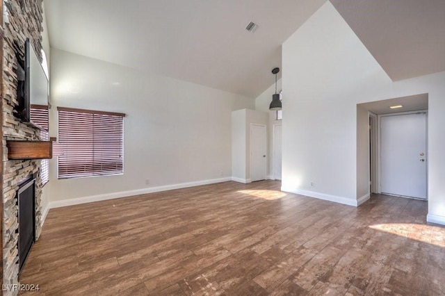 unfurnished living room featuring hardwood / wood-style floors, high vaulted ceiling, and a stone fireplace