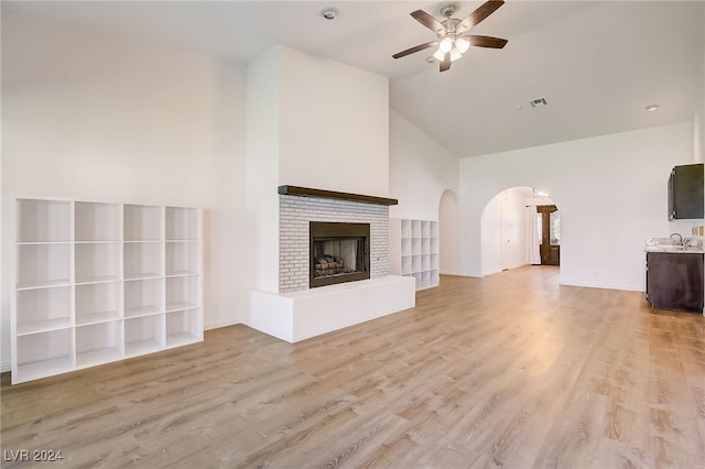 unfurnished living room featuring ceiling fan, light wood-type flooring, a fireplace, and high vaulted ceiling