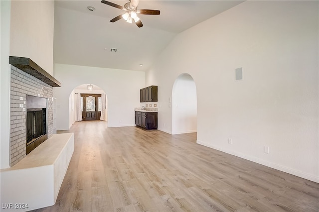 unfurnished living room with ceiling fan, high vaulted ceiling, light hardwood / wood-style floors, and a brick fireplace