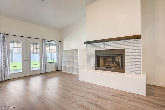 unfurnished living room with lofted ceiling, french doors, a fireplace, and light hardwood / wood-style flooring