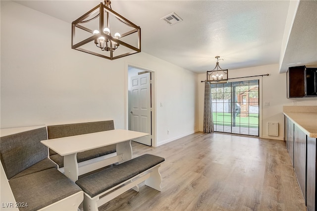 unfurnished dining area featuring light hardwood / wood-style flooring, a textured ceiling, and an inviting chandelier