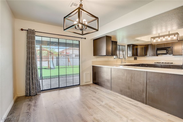 kitchen with dark brown cabinetry, sink, hanging light fixtures, an inviting chandelier, and light wood-type flooring