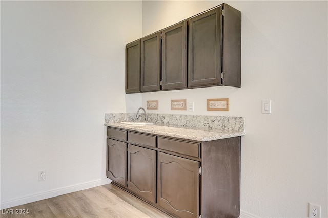 bar with sink, dark brown cabinets, and light wood-type flooring