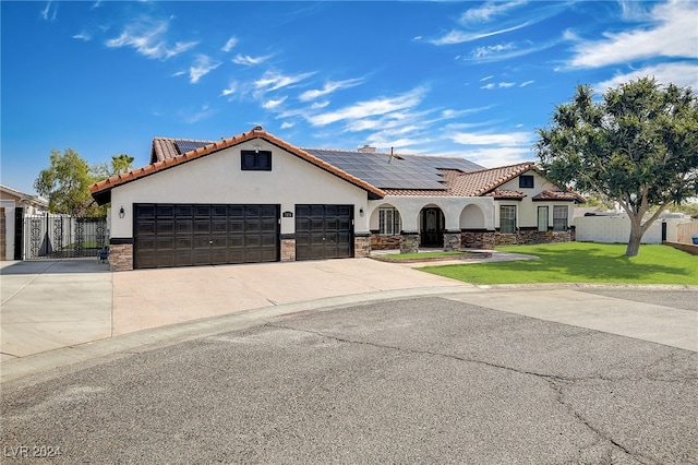 mediterranean / spanish-style home featuring a garage, a front yard, and solar panels