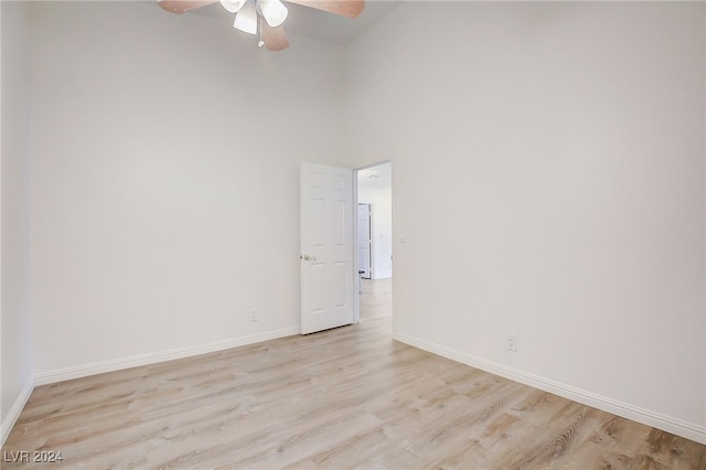 spare room with ceiling fan, a towering ceiling, and light wood-type flooring