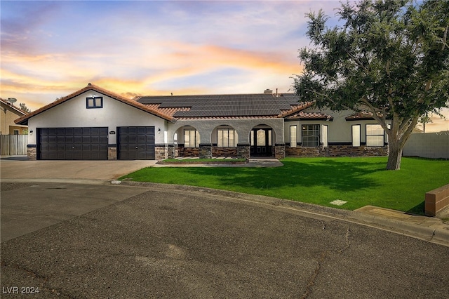 mediterranean / spanish house with solar panels, a garage, and a lawn