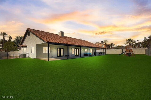 back house at dusk with a playground and a lawn