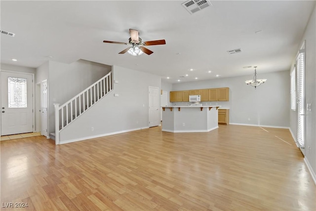 unfurnished living room with ceiling fan with notable chandelier and light wood-type flooring