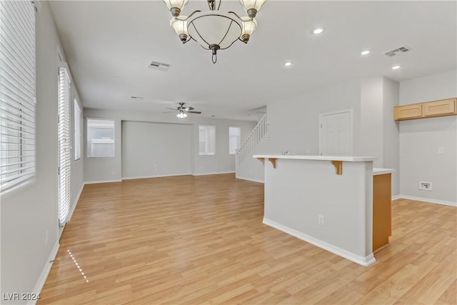 unfurnished living room with ceiling fan with notable chandelier and light wood-type flooring