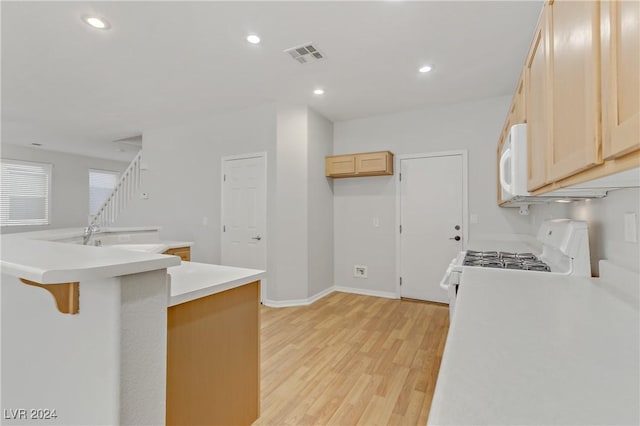 kitchen with light brown cabinets, light hardwood / wood-style flooring, kitchen peninsula, white appliances, and a breakfast bar