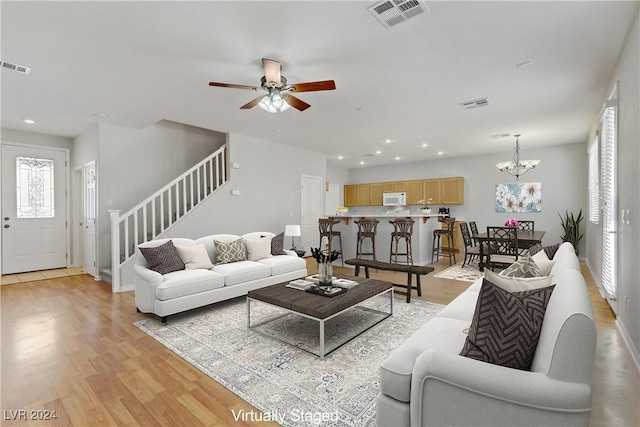 living room with ceiling fan with notable chandelier and light wood-type flooring