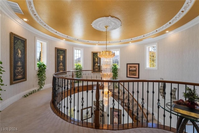 corridor featuring a textured ceiling, a raised ceiling, crown molding, a notable chandelier, and carpet floors