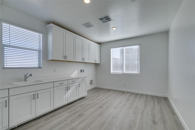 kitchen with light wood-type flooring, white cabinetry, and sink