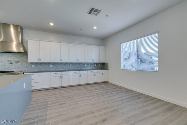 kitchen with light stone countertops, white cabinets, light hardwood / wood-style floors, and wall chimney range hood