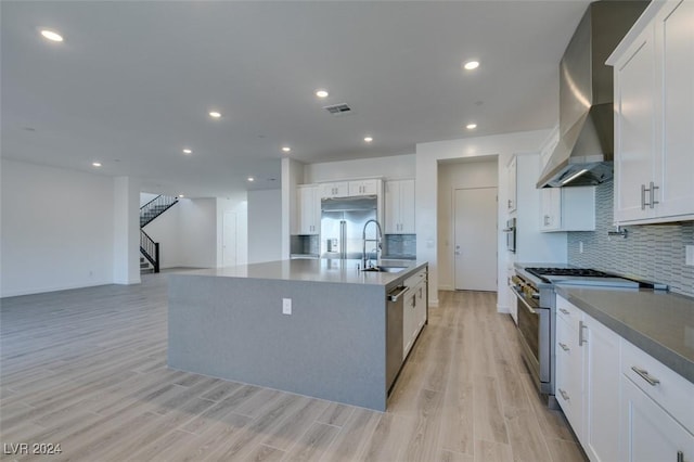 kitchen featuring wall chimney range hood, sink, premium appliances, light hardwood / wood-style floors, and white cabinetry