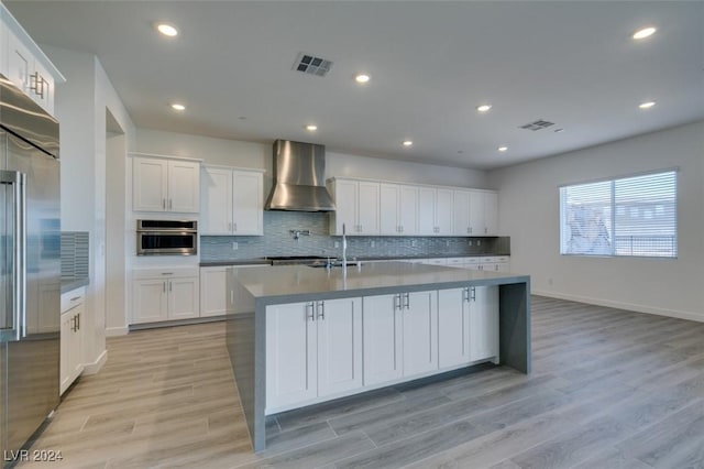 kitchen with appliances with stainless steel finishes, light hardwood / wood-style floors, white cabinetry, and wall chimney range hood