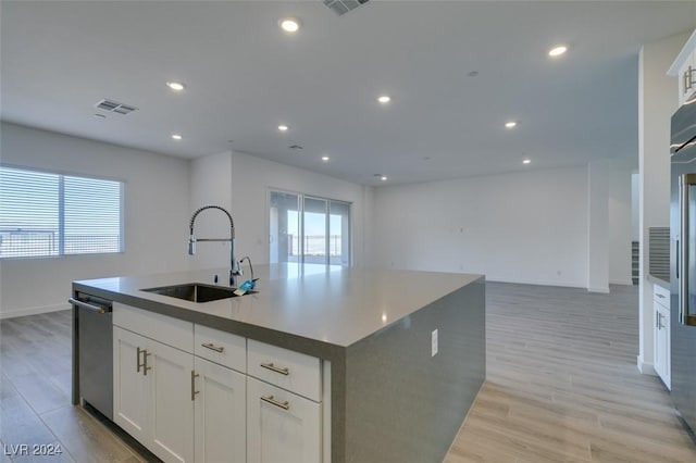 kitchen featuring stainless steel dishwasher, sink, a center island with sink, light hardwood / wood-style flooring, and white cabinets