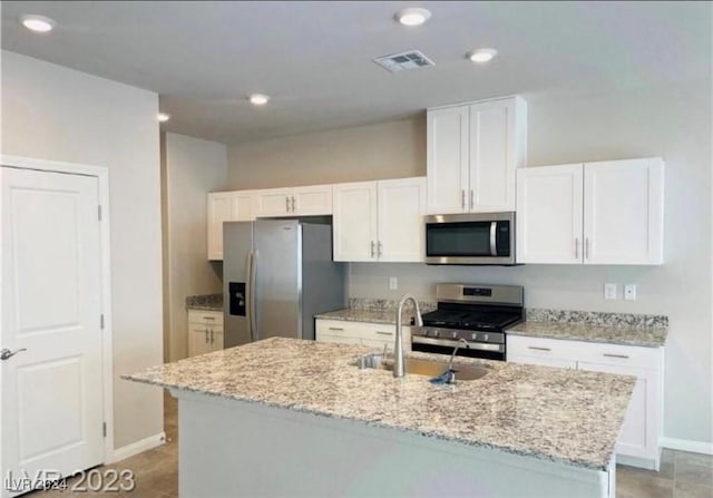 kitchen featuring sink, white cabinetry, stainless steel appliances, light stone countertops, and an island with sink