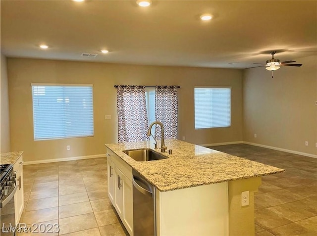 kitchen featuring sink, appliances with stainless steel finishes, white cabinetry, light stone countertops, and a center island with sink