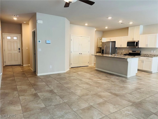 kitchen featuring appliances with stainless steel finishes, an island with sink, white cabinets, ceiling fan, and light stone countertops