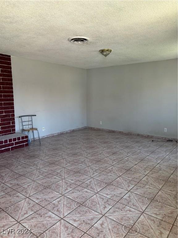 tiled empty room featuring visible vents and a textured ceiling