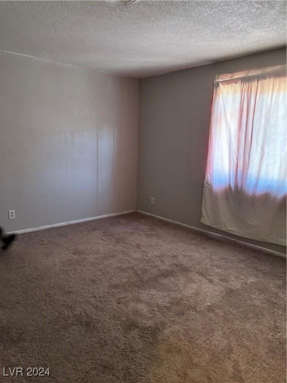 empty room with carpet flooring, baseboards, and a textured ceiling