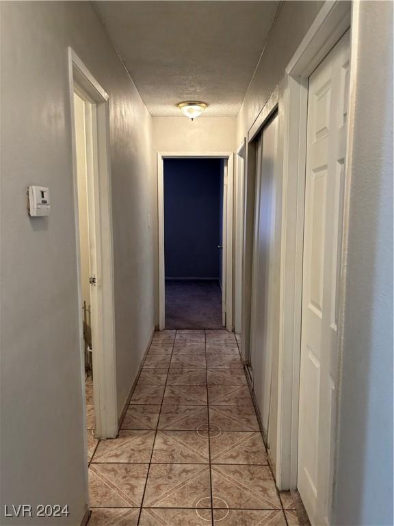 corridor with a textured ceiling and light tile patterned flooring