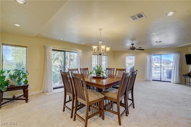 dining space with a wealth of natural light, light colored carpet, and ceiling fan with notable chandelier