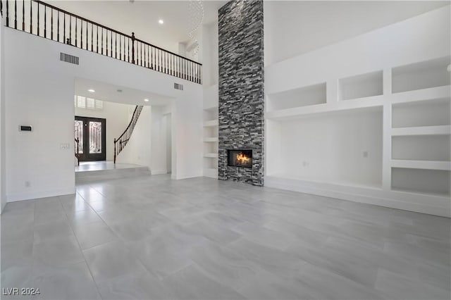 unfurnished living room with french doors, a towering ceiling, built in features, and a stone fireplace