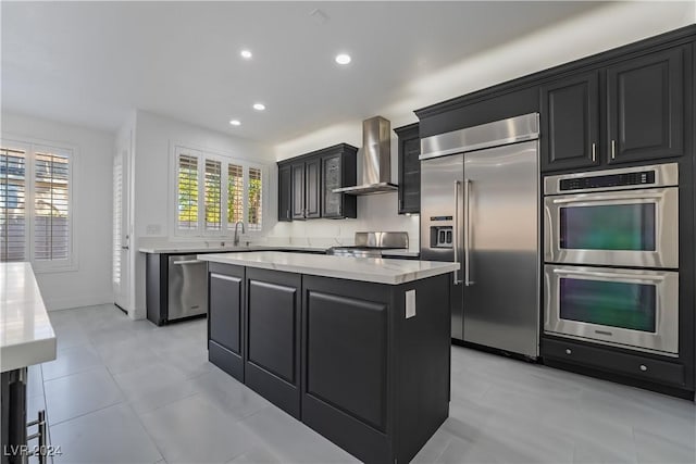 kitchen with appliances with stainless steel finishes, a center island, light tile patterned floors, and wall chimney exhaust hood