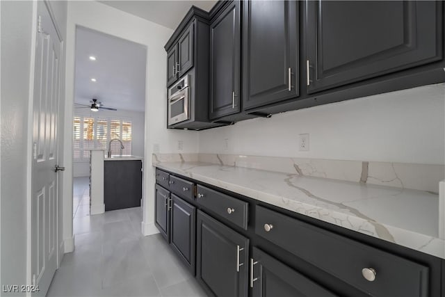 kitchen with ceiling fan, light stone counters, and sink