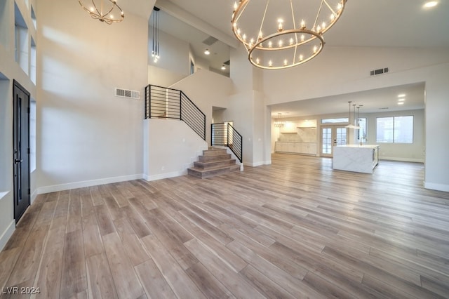 unfurnished living room with french doors, light wood-type flooring, an inviting chandelier, and high vaulted ceiling