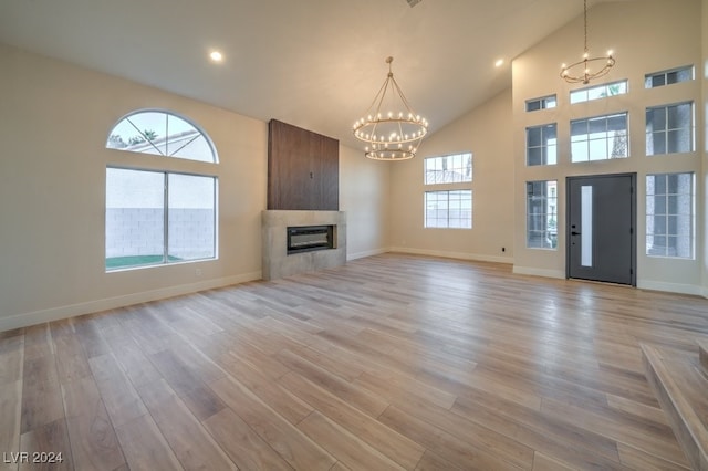 unfurnished living room with a chandelier, a tiled fireplace, high vaulted ceiling, and light hardwood / wood-style flooring