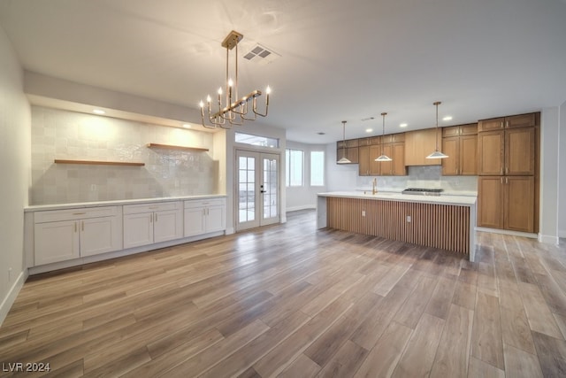 kitchen featuring french doors, tasteful backsplash, decorative light fixtures, hardwood / wood-style flooring, and a center island with sink