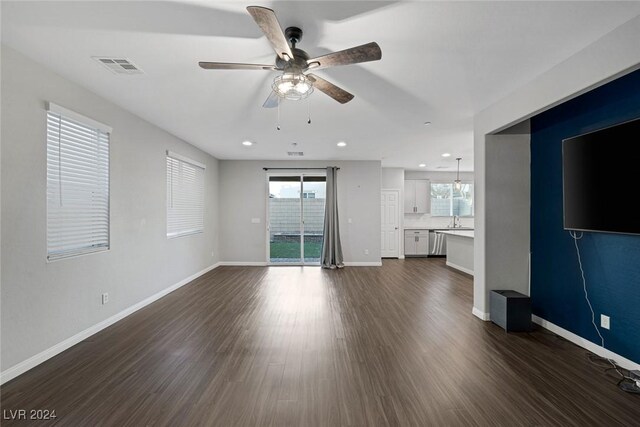 unfurnished living room featuring ceiling fan with notable chandelier, plenty of natural light, and dark hardwood / wood-style flooring