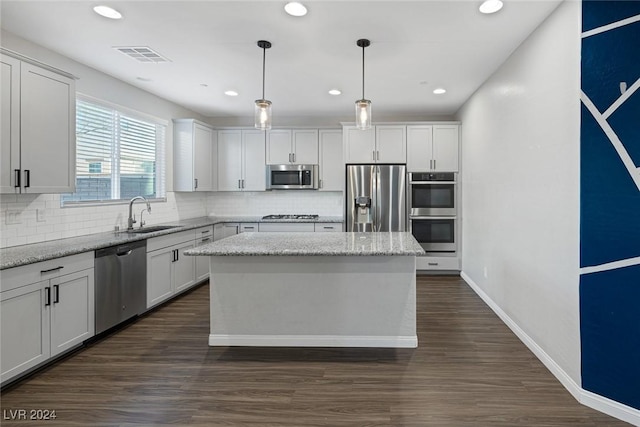 kitchen with light stone countertops, appliances with stainless steel finishes, a kitchen island, decorative light fixtures, and sink