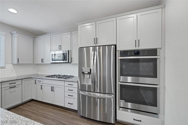 kitchen with light stone countertops, white cabinets, dark hardwood / wood-style floors, and stainless steel appliances