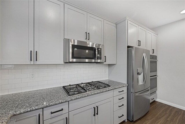 kitchen featuring tasteful backsplash, white cabinetry, light stone countertops, appliances with stainless steel finishes, and dark hardwood / wood-style flooring