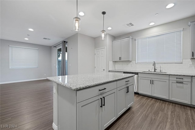 kitchen with decorative backsplash, light stone counters, hanging light fixtures, and sink